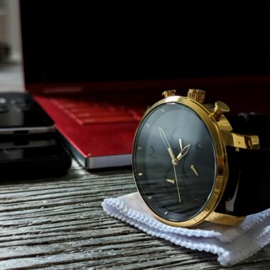 Elegant gold wristwatch placed on a stylish wooden surface with a laptop in the background.