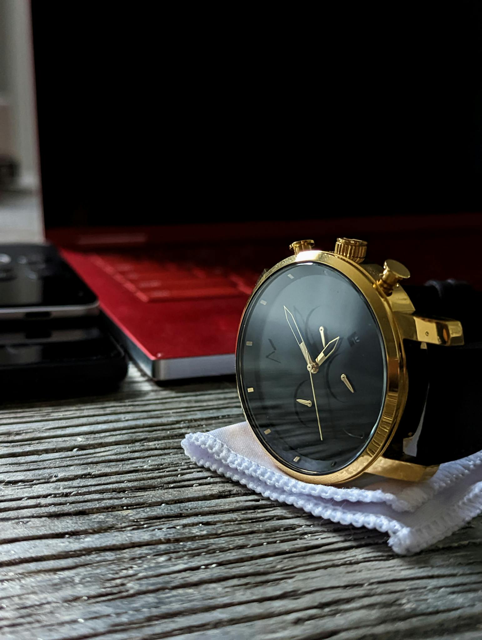 Elegant gold wristwatch placed on a stylish wooden surface with a laptop in the background.